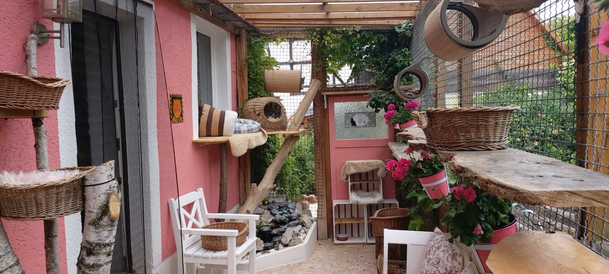 Außengehege mit rosafarbener Wand, Wasserlauf mit Kieseln und weißem Stuhl